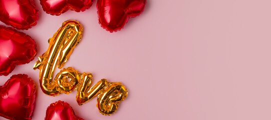Foil balloons in the shape of a heart and a balloon from the letters LOVE on a pink background. Copy Space.