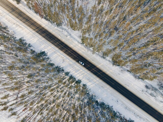 Aerial drone view of road with moving car in idyllic winter landscape. Nature from a birds eye view.