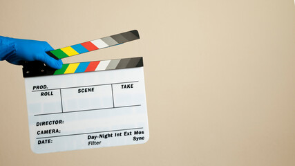 Hand in blue surgical glove hitting a movie clapperboard on neutral background. Film set with...