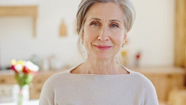 Natural beauty of aging. Peaceful positive senior lady looking at camera, posing at home interior with flowers bouquet