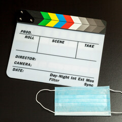 Face protection mask with clapper board on the table on black background. Audiovisual protection...