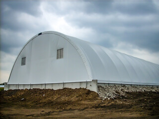 Prefabricated hoop barn with a tarp covering against a cloudy sky. 