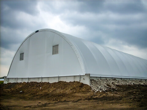 Prefabricated Hoop Barn With A Tarp Covering Against A Cloudy Sky. 