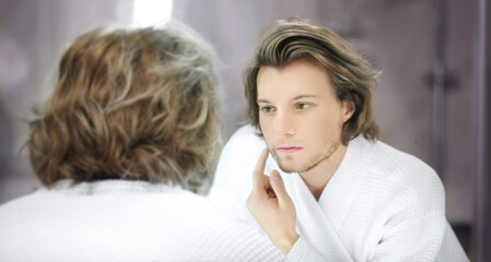 young man looking in the mirror,combing his hair,looking at problems on face.