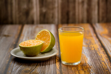 Orange juice. Glass on wooden table with a sliced orange in the background.