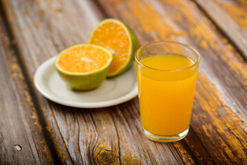 Orange juice. Glass on wooden table with a sliced orange in the background.