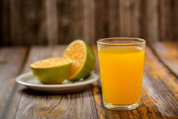 Fototapeta premium Orange juice. Glass on wooden table with a sliced orange in the background.
