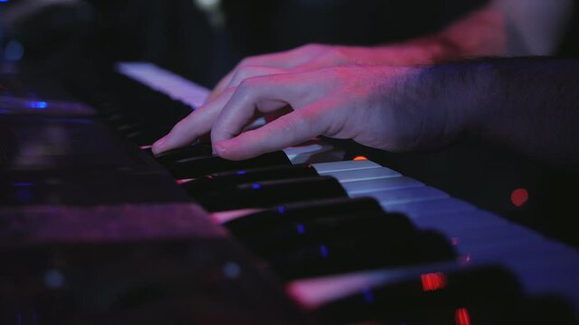 A male musician plays a synthesizer on stage, close-up.