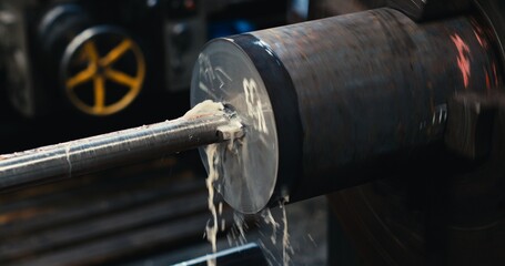 A close-up of a metal workpiece clamped in a rotating chuck of a machine tool. Steel drill and shavings. Detail of drilling on a lathe with metal shavings.