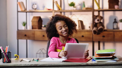 cheerful african american girl using digital tablet near notebooks on desk.