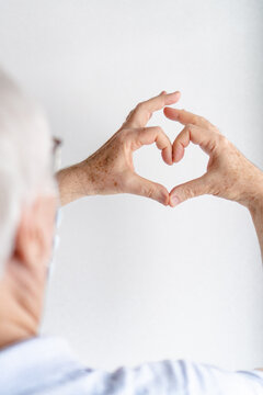 older man making a heart with his hands, white background, wearing a medical mask, vertical photo