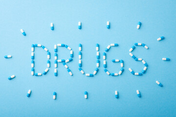 Word Drugs made of pills on blue background. Concept of treatment, tablets