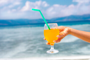 a picture of a hand with a cocktail in the background of a tropical beach; the hand holding a bright cocktail against the background of a tropical beach