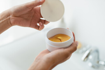 Cropped view of african american woman holding jar with hydrogel eye patches in bathroom.