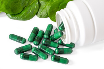 Green supplement capsules with spinach leaves on white.
