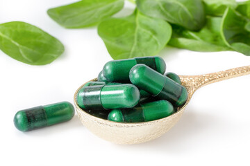 Green supplement capsules with spinach leaves on white.