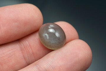 Oval cabochon moonstone. Gray base, black inclusions dots, spots. Semitransparent, translucent oval...