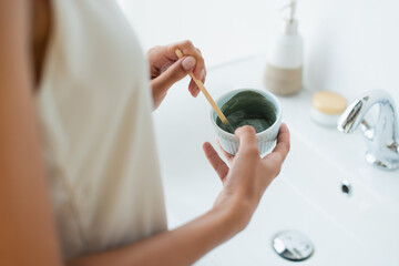 Cropped view of african american woman in nightgown mixing face mask in bathroom.