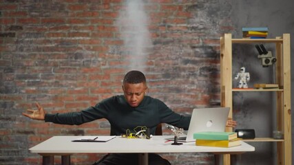 Emotional African-American man scientist with steam rising above head with boiled brains angry of failed experiment puts up hands at table with notebook