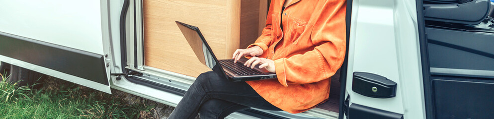 Woman teleworking sitting in the door of a camper van while her partners work inside