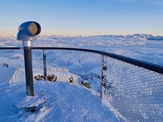 Coin binoculars on visitors' platform of Hoher Kasten cable car mountain station, spectacular mountain panorama on sunny winter day. Alpstein, Appenzell, Switzerland.