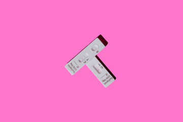 Overhead view of two covid-19 antigen rapid diagnostic test devices, the top one with a positive result and the bottom one with a negative result, on a pink background