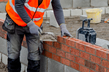 Bricklayer laying bricks on mortar on new residential house construction - obrazy, fototapety, plakaty