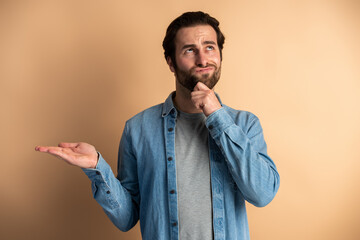 Portrait of young pensive man with beard touching chin and thinking about important question