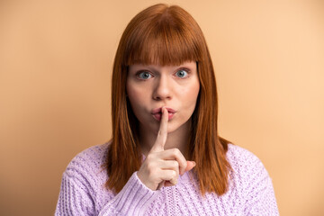 Serious woman showing silence gesture with finger on her mouth, asking to stay quiet, keep secret