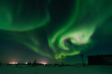 The northern lights and aurora borealis fill the sky above distant city lights near Churchill, Manitoba, Canada