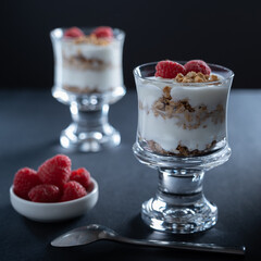 Two glass bowls of vanilla yogurt with cinnamon roll granola and raspberry topping