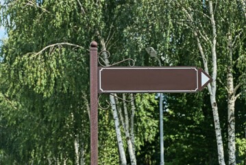 one brown iron arrow pointer on an iron pole in a park against a background of green vegetation