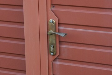 one gray brown metal doorknob on a red closed iron door on the street