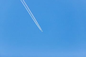 Airliner in the blue sky without clouds. There are engine tracks behind the plane