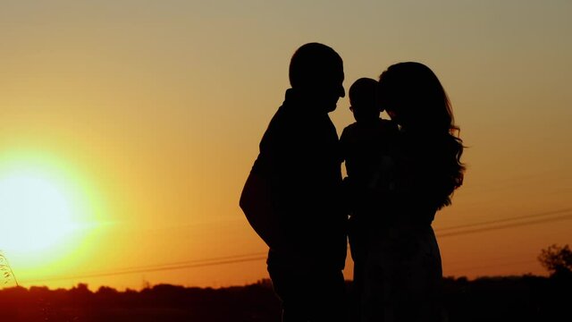 Unrecognizable silhouette of family at sunset, parents hug and kiss their child, family values and parental love