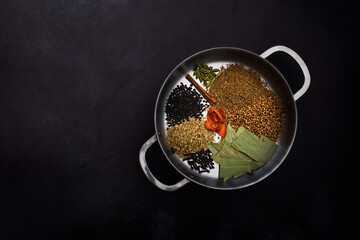 Indian curry spices arranged in a metal pan and placed on right side of frame. Plain dark background, natural lighting, with copy space available.