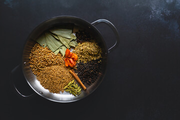 Indian curry spices arranged in a metal pan against a plain dark background with copy space...