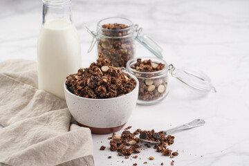 Breakfast muesli cereal with chocolate chips and nuts in several jars and bowl, bottle of milk,...