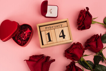 top view of red roses near calendar with 14 february lettering, confetti and engagement ring on pink.
