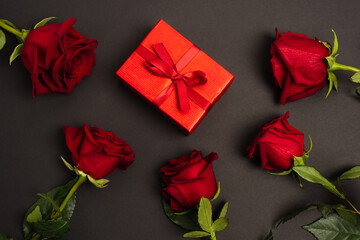 flat lay of red roses near wrapped gift box on black.