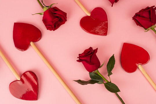 top view of heart-shaped lollipops near red roses on pink.