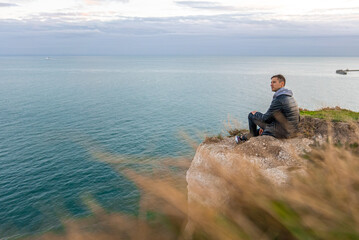 Young man exploring the White Cliffs of Dover in UK. Sitting on top of the cliff watching English...