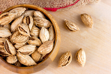 Top view of roasted brown almond nuts in cracked shell in wooden bowl on light table background ready to eat.