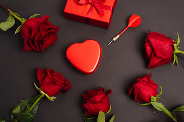 flat lay of metallic heart-shaped box near wrapped present, dark and roses, on black.