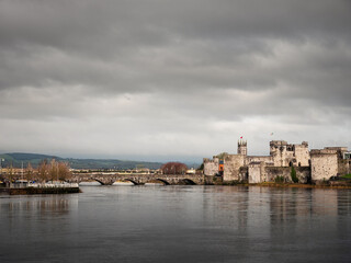 Fototapeta na wymiar King Jonh's castle on River Shannon, Limerick city, Ireland. Popular museum and landmark. Fine example of stone stronghold with tall walls and towers. Cloudy sky. Building reflection in water.