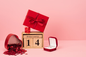 red gift boxes on calendar with 14 february near engagement ring and confetti on pink.