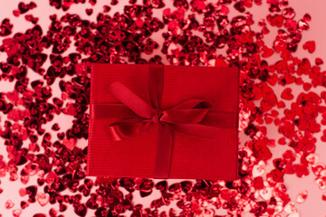 top view of wrapped present near shiny red confetti hearts on pink.