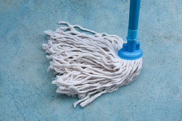 Mop with PVC blue handle standing on cement flooring background closeup to clean hygiene.