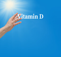 Get your Vitamin D in the Sunshine background - female hands reaching out to take the words Vitamin D against a rich blue sky and sun shining with copy space
