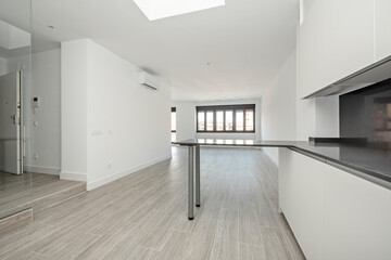 Kitchen with white cabinets, black countertops, island of the same material and window in the background